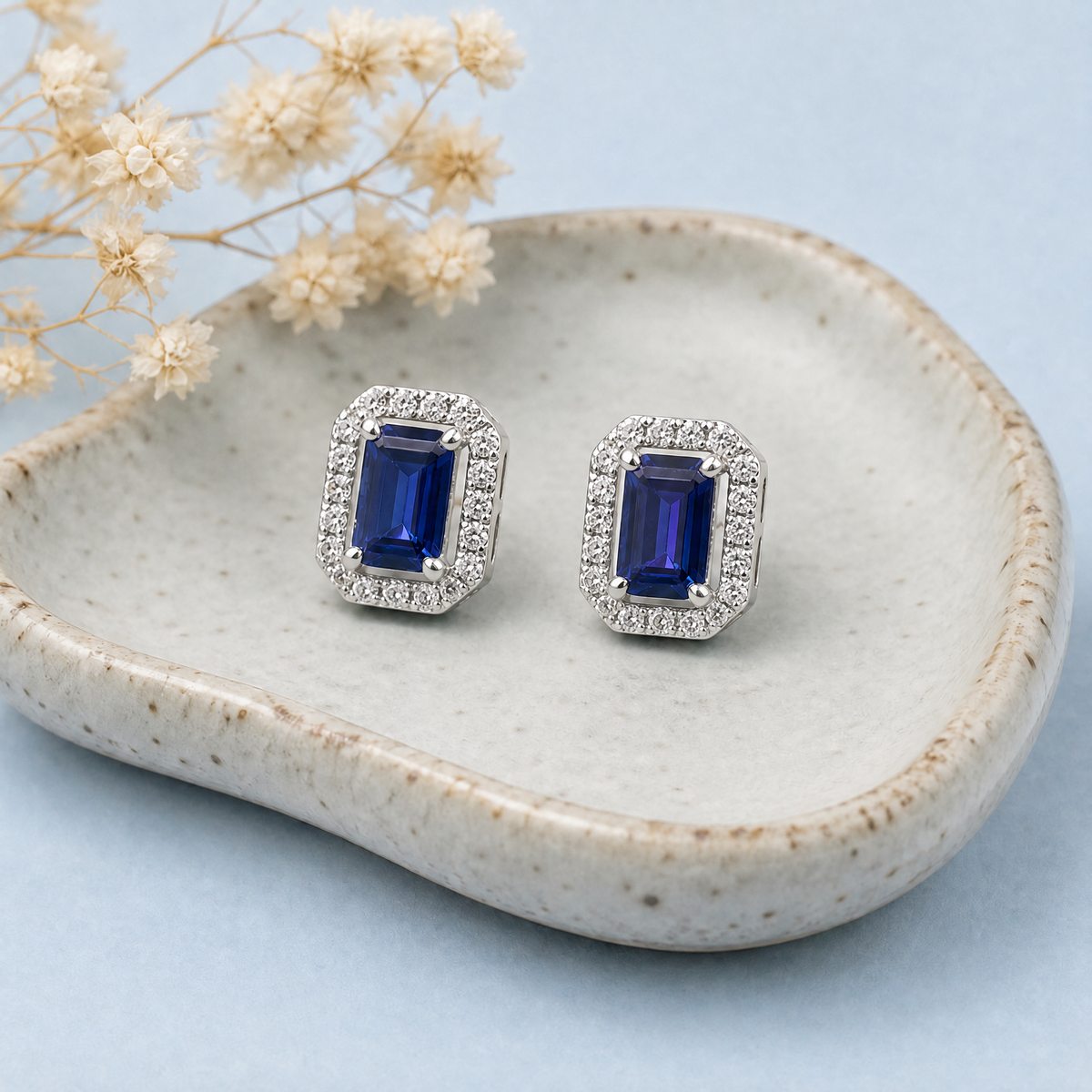 Blue Step Cut Halo Stud Earrings in 925 sterling silver, on a ceramic dish